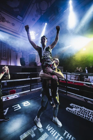 A winner lifted up in the ring under the ballroom lights