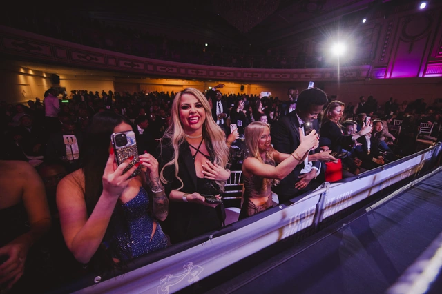 Women in evening wear cheering and filming at the ringside barrier