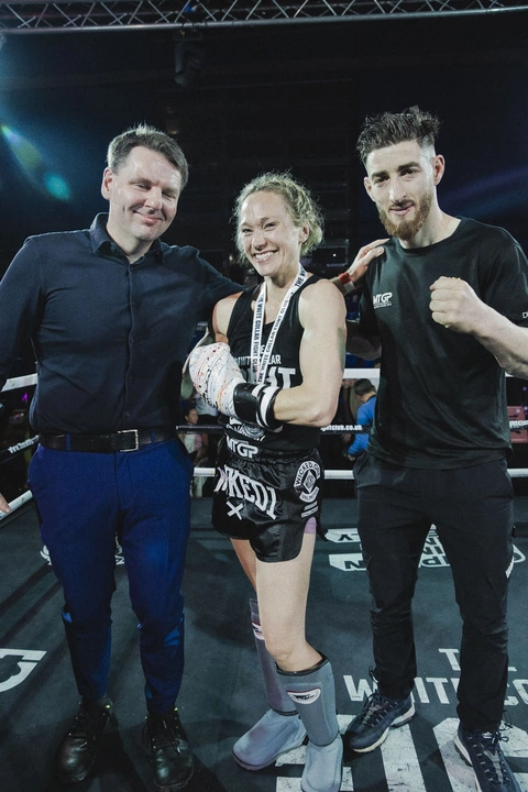 Donna stands in the ring in her White Collar Fight Club vest and shin guards after her fight