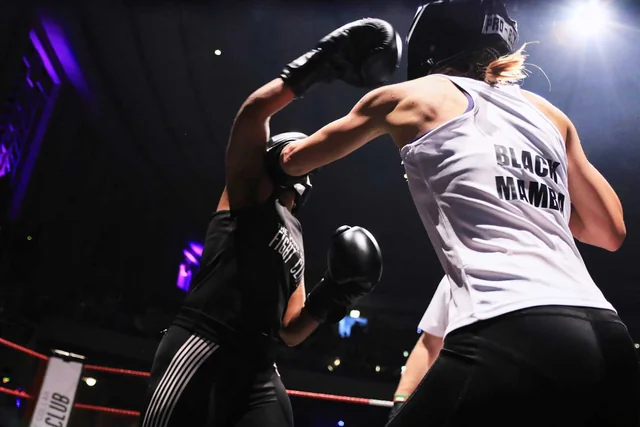 Two fighters in head guards trade punches under purple lights at Gemma's fight night
