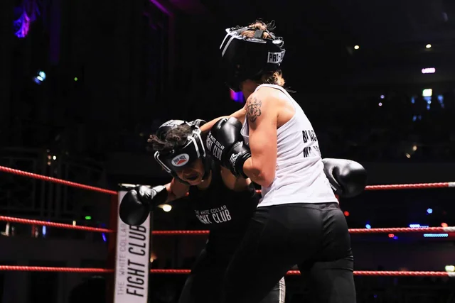 Two fighters in head guards work at close range in the ring