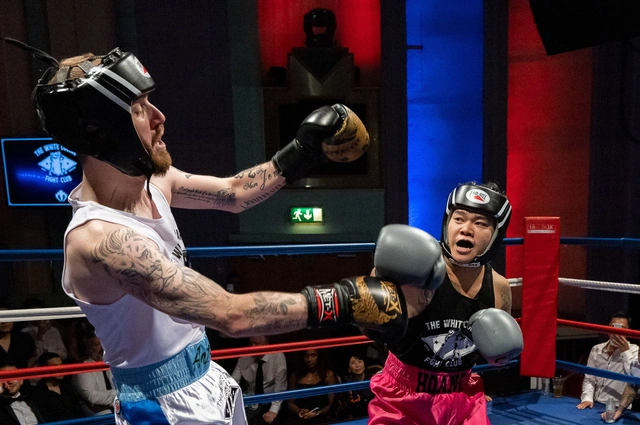 A tattooed boxer in a white vest throws a right hand while his opponent in pink shorts slips it