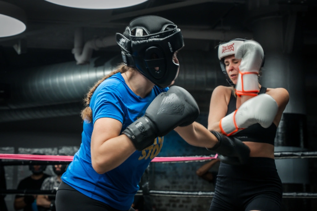 Two women in head guards sparring in a boxing session