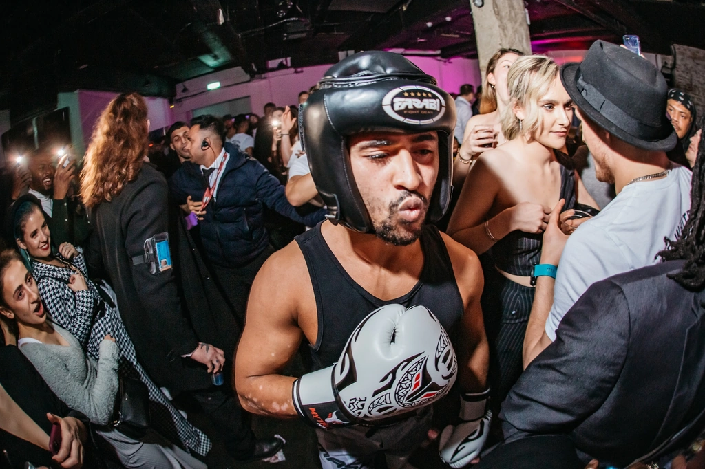 A fighter in a head guard making his ring walk through a packed Backyard Bouts crowd