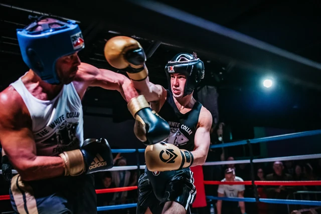 Two boxers in head guards exchanging punches under the lights on fight night