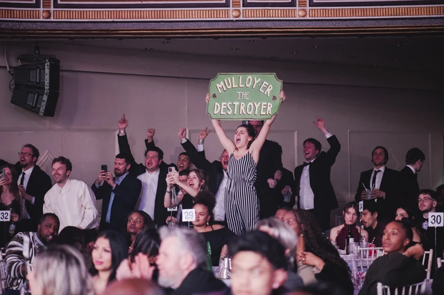 Supporters in black tie on their feet cheering with a homemade sign