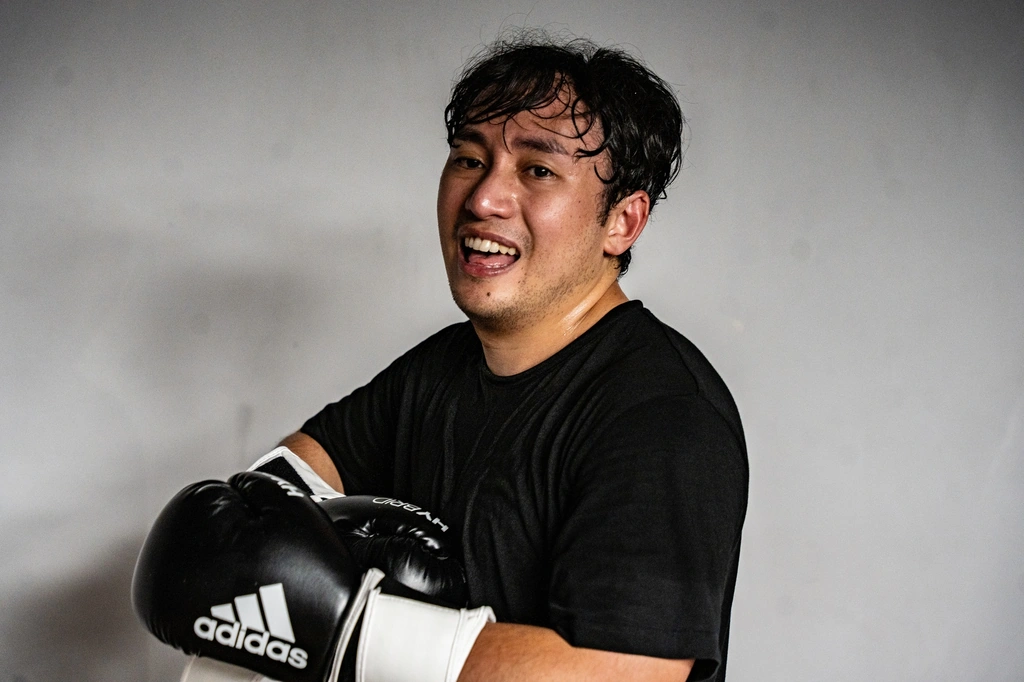 A smiling fighter in a black T-shirt pulling on his boxing gloves