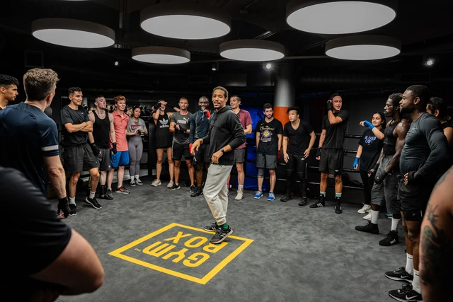 A coach talking to a circle of new fighters on the Gymbox floor